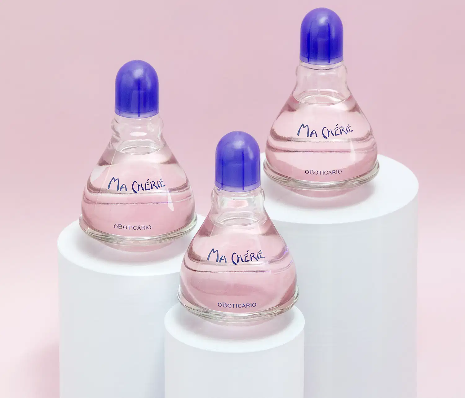 Três vidros transparentes com fundos arredondados, líquidos rosas, tampas e letras azuis de desodorante colônia Ma Chérie. dispostos em pedestais brancos contra fundo rosa claro.