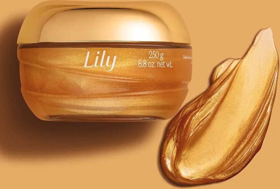 Pote de vidro transparente com creme dourado, tampa dourada e letras bege de geleia iluminadora corporal da marca Lily Glow em fundo bege, acompanhado de amostra de produto com textura dourada e brilhante ao lado.