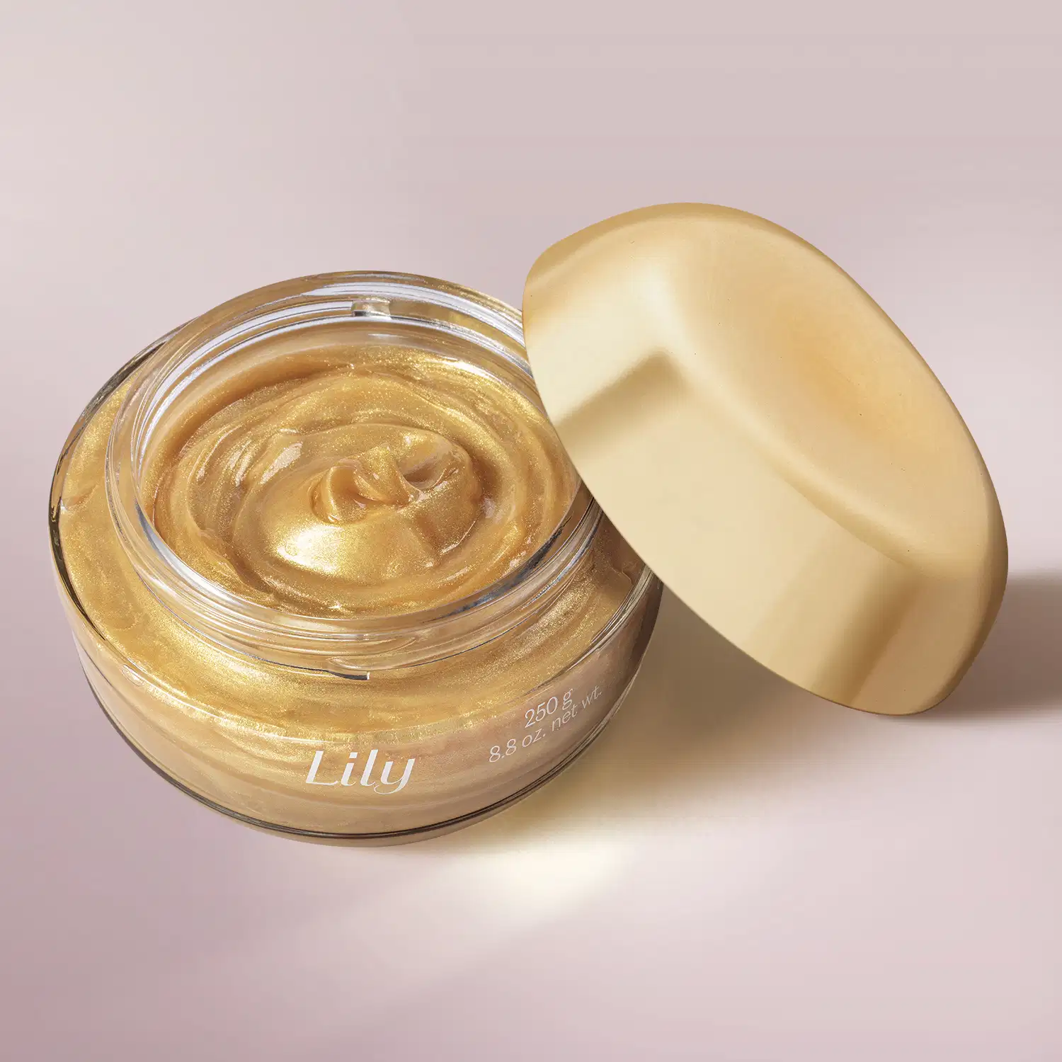 Pote de vidro transparente aberto mostrando o creme dourado da geleia iluminadora corporal da marca Lily Glow, com a tampa dourada encostada na embalagem, .