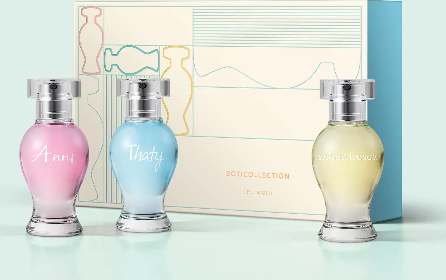 Três vidros curvilíneos com borrifador prateado e tampa cristal de desodorante colônia Boticollection em versão miniatura, sendo um da marca Anni, outro da marca Thaty e a outra da marca Acqua Fresca, junto com uma caixa de presente em fundo azul claro.