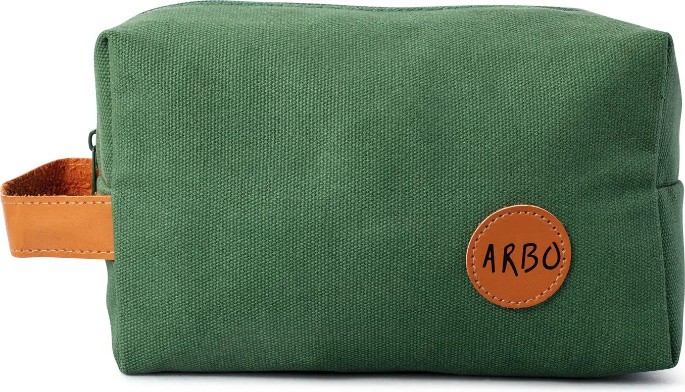 Nécessaire retangular de lona verde com alça de couro caramelo e logo Arbo em patch circular também em couro caramelo.