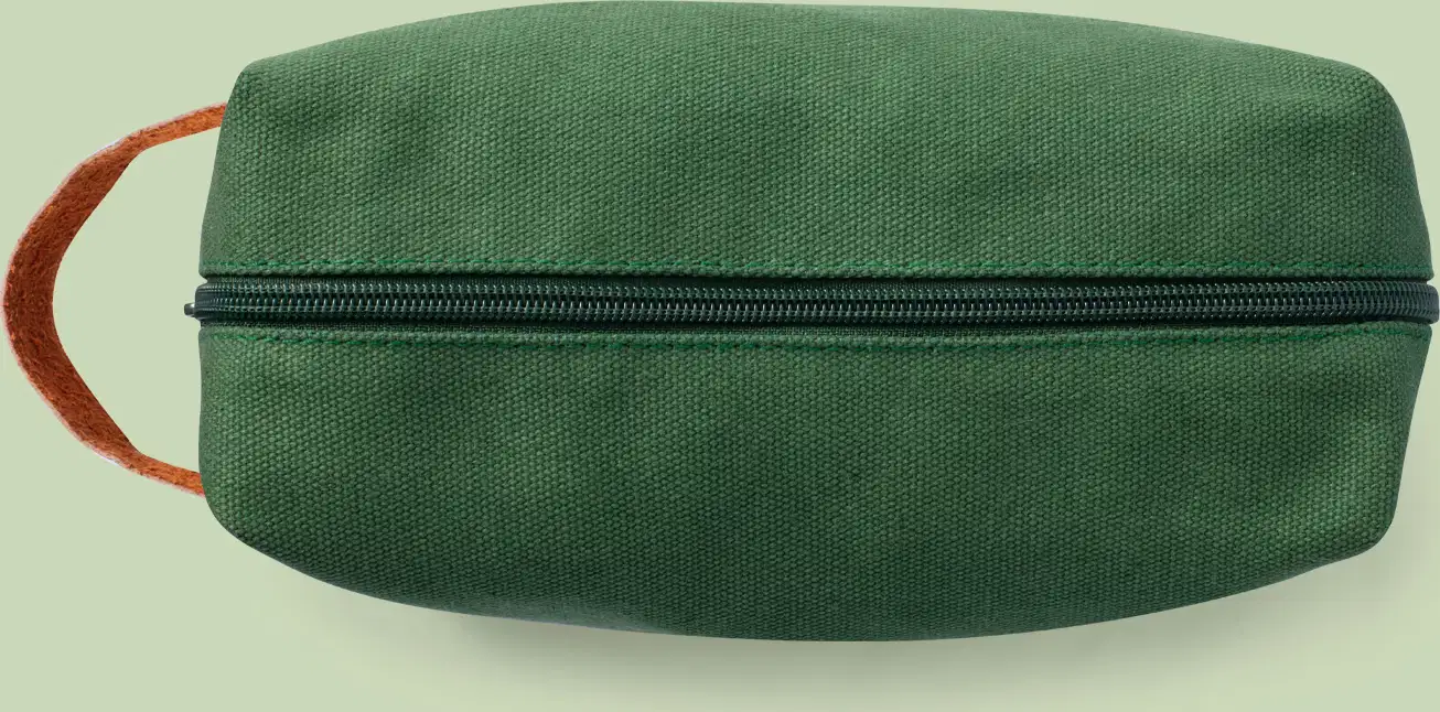 Nécessaire retangular de lona verde com alça de couro caramelo e zíper verde.