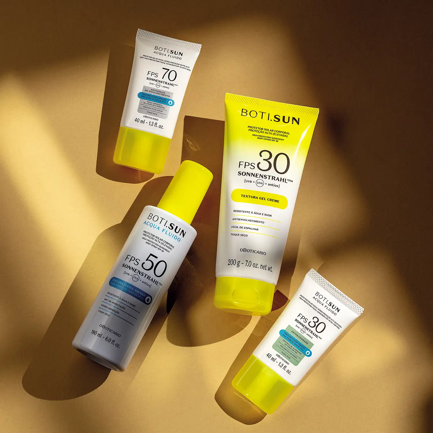 Quatro produtos Boti Sun com protetor solar em embalagens brancas e amarelas dispostos sobre superfície bege com sombras, apresentando FPS 70, 50 e 30, em diferentes formatos de tubo e frasco.