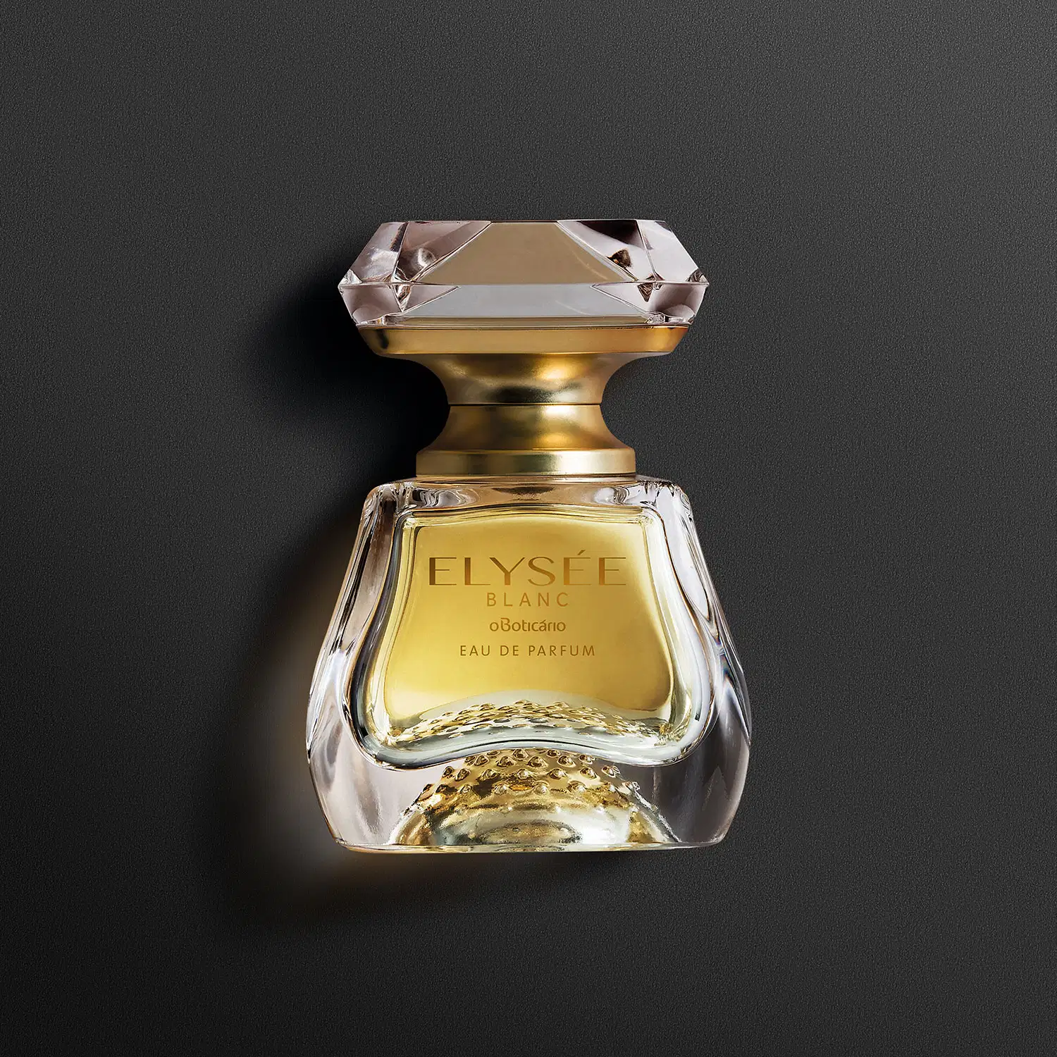 Vidro transparente com líquido bege, pulverizador dourado e tampa transparente simulando um cristal lapidado de Eau de Parfum Elysée Blanc em fundo escuro.