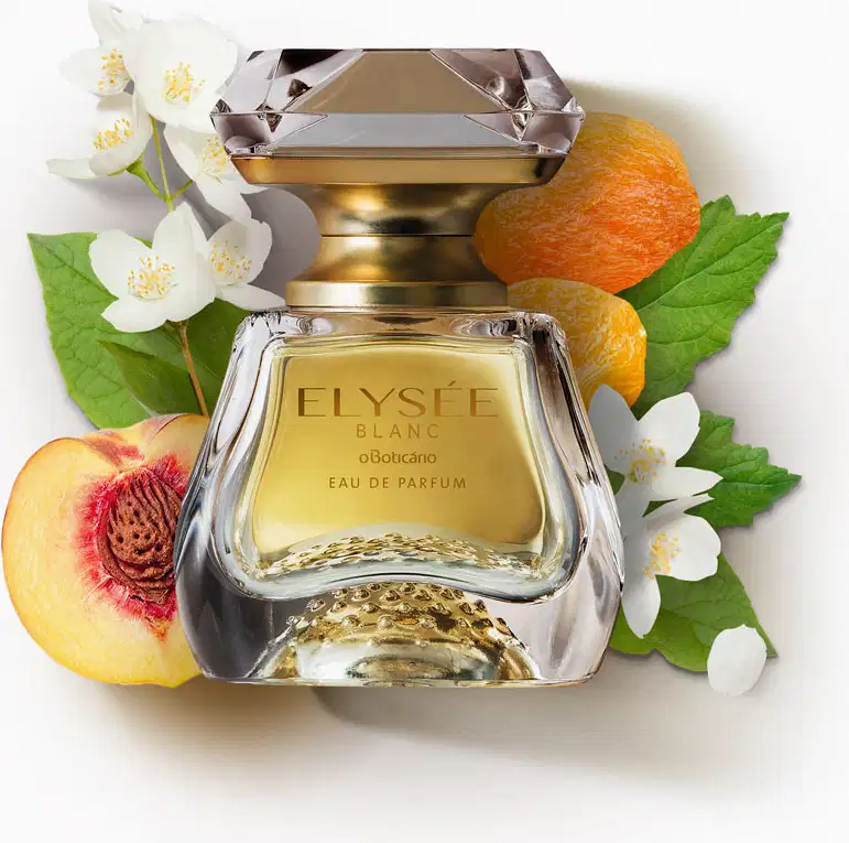 Vidro transparente com líquido bege, pulverizador dourado e tampa transparente simulando um cristal lapidado de Eau de Parfum Elysée Blanc cercado por flores brancas, pêssego cortado, laranjas e folhas verdes sobre superfície branca.