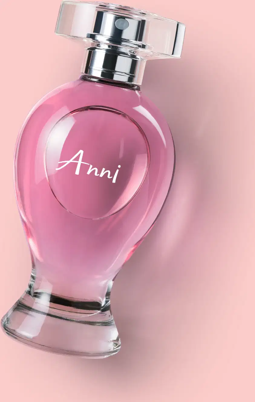 Vidro curvilíneo transparente com liquido rosa, pulverizador prateado e tampa cristal contendo desodorante colônia Boticollection Anni deitado em um fundo rosa.