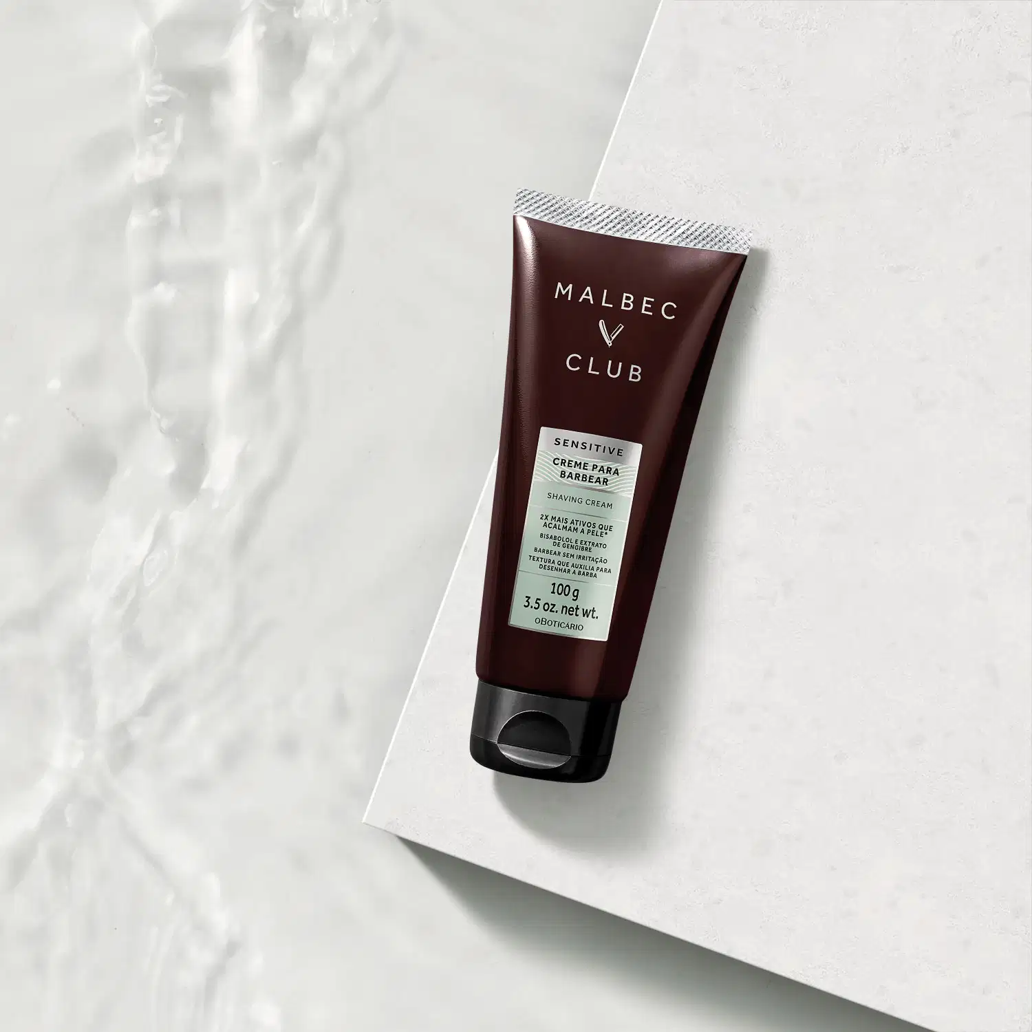 Tubo de creme para barbear da marca Malbec Club em fundo branco com textura de mármore. O cenário sugere um ambiente minimalista e elegante, adequado para o uso deste item de perfumaria.
