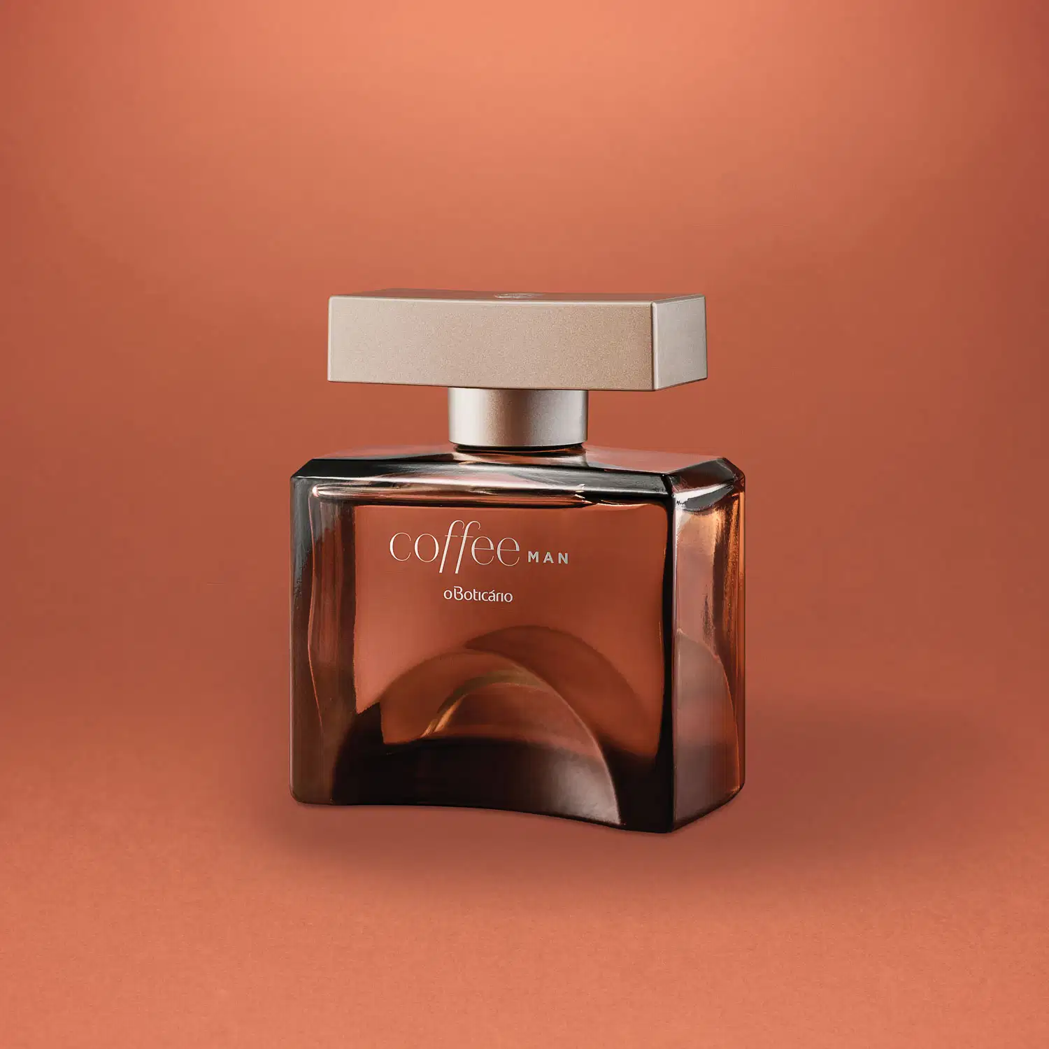 Frasco quadrado marrom com tampa retangular na mesma cor e letras cinzas, contendo desodorante colônia Coffee Man Seduction em fundo em tons de laranja.