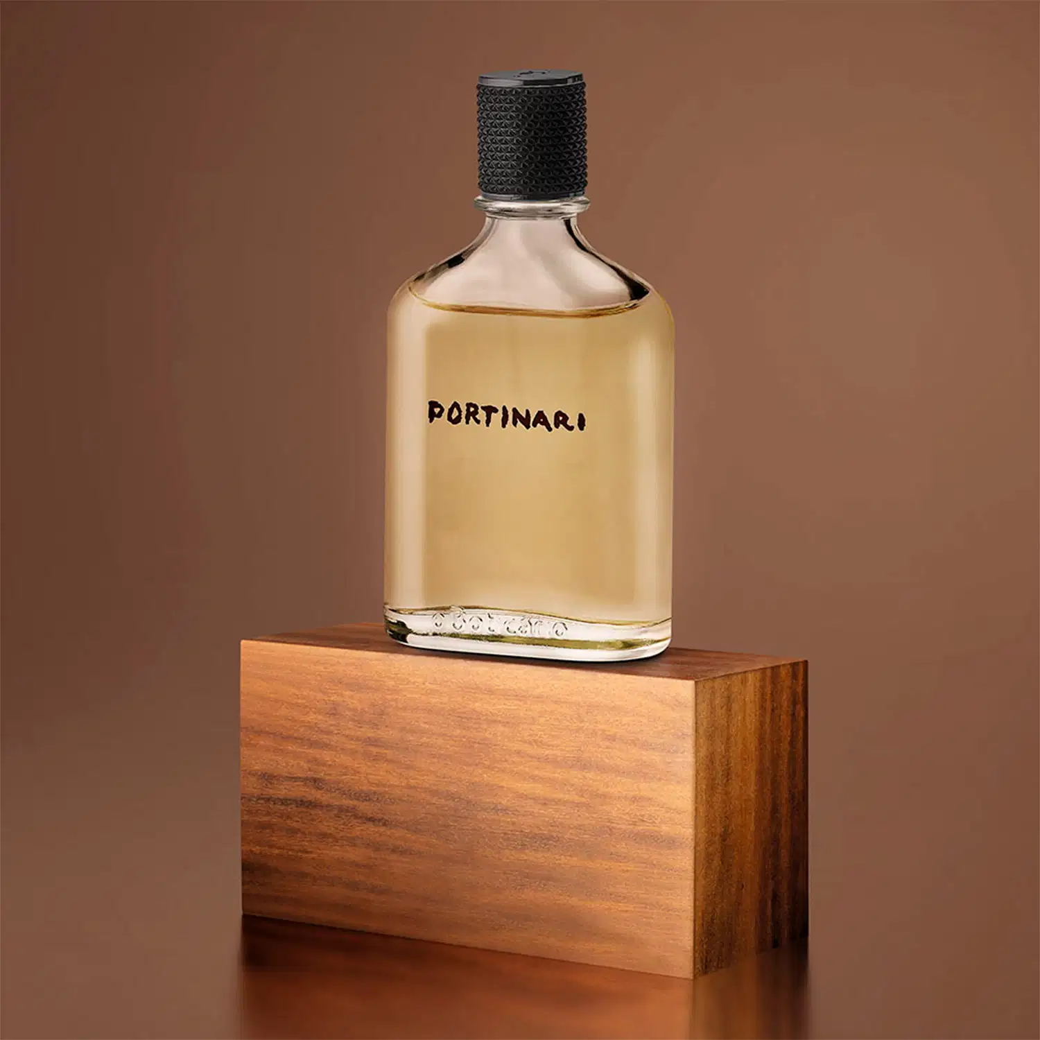 Frasco transparente com líquido bege, tampa preta e letras marrons contendo 100ml de desodorante colônia Boticollection Portinari em superfície de madeira e em fundo marrom.