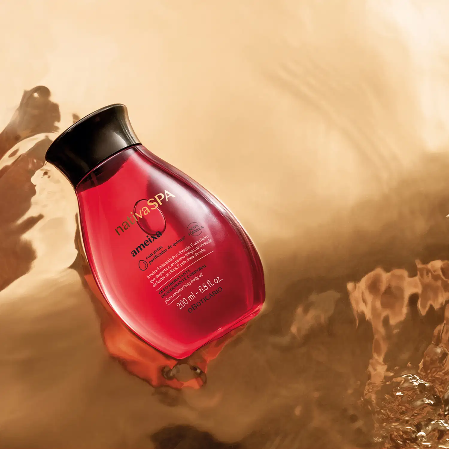 Frasco transparente rosa com líquido rosado, tampa preta e letras douradas, pretas e cinzas de óleo hidratante corporal da marca Nativa SPA Ameixa, posicionado em superfície com rochas e areia em tons bege e marrom, sob iluminação natural quente.