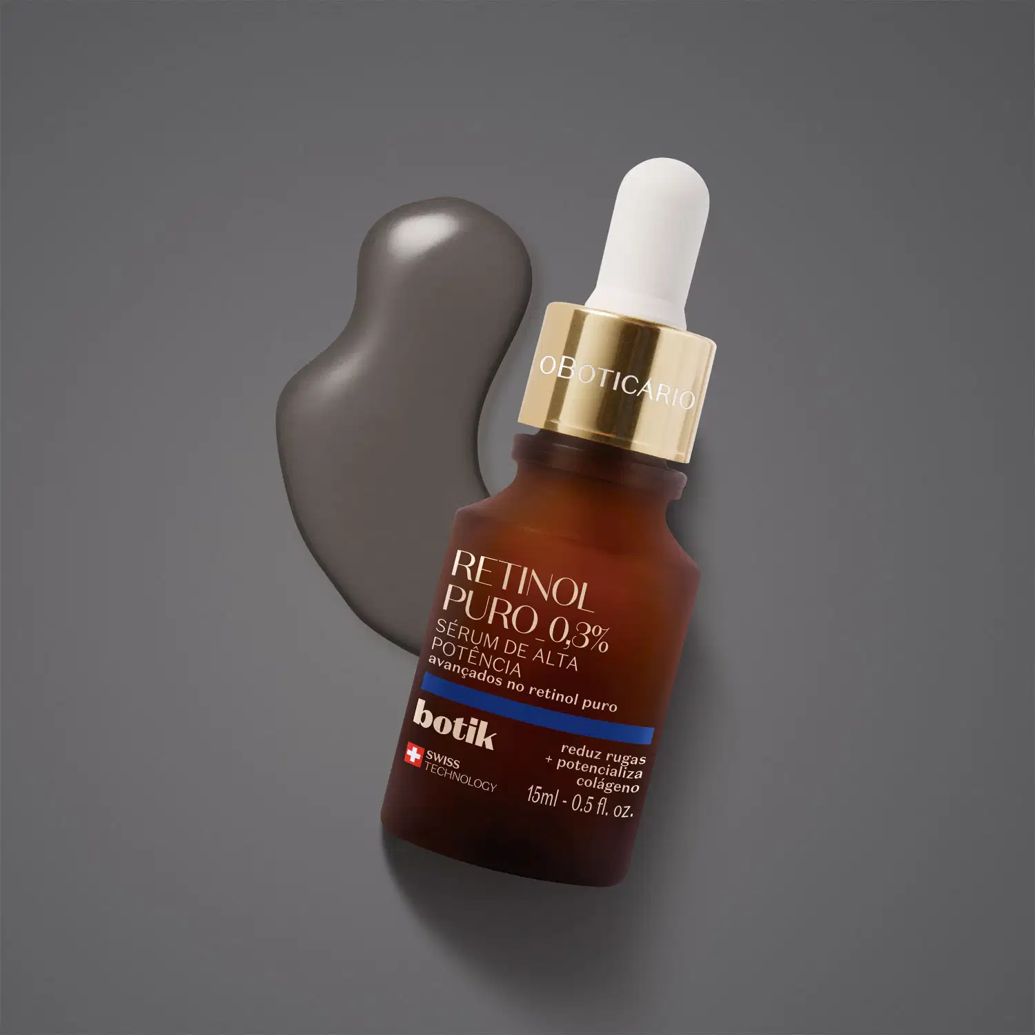 Vidro marrom com tampa dourada, conta-gotas branco, letras bege e detalhe azul contendo 15ml de sérum facial de alta potência Botik Retinol Puro sobre fundo cinza e uma pequena quantidade do produto espalhada atrás da embalagem.