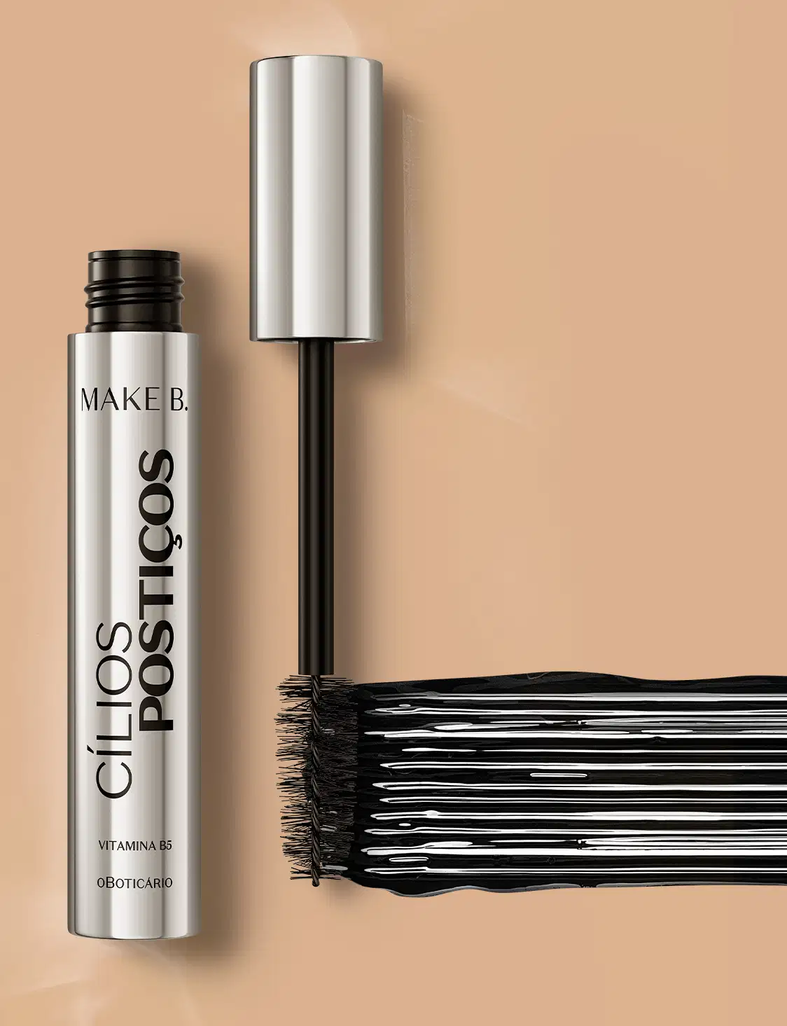 Tubo prateado com tampa na mesma cor, letras, haste e escova aplicadora pretas, contendo 10g de máscara de cílios Make B. Efeito Cílios Postiços. Há um rastro do produto mostrando a cor e a intensidade.