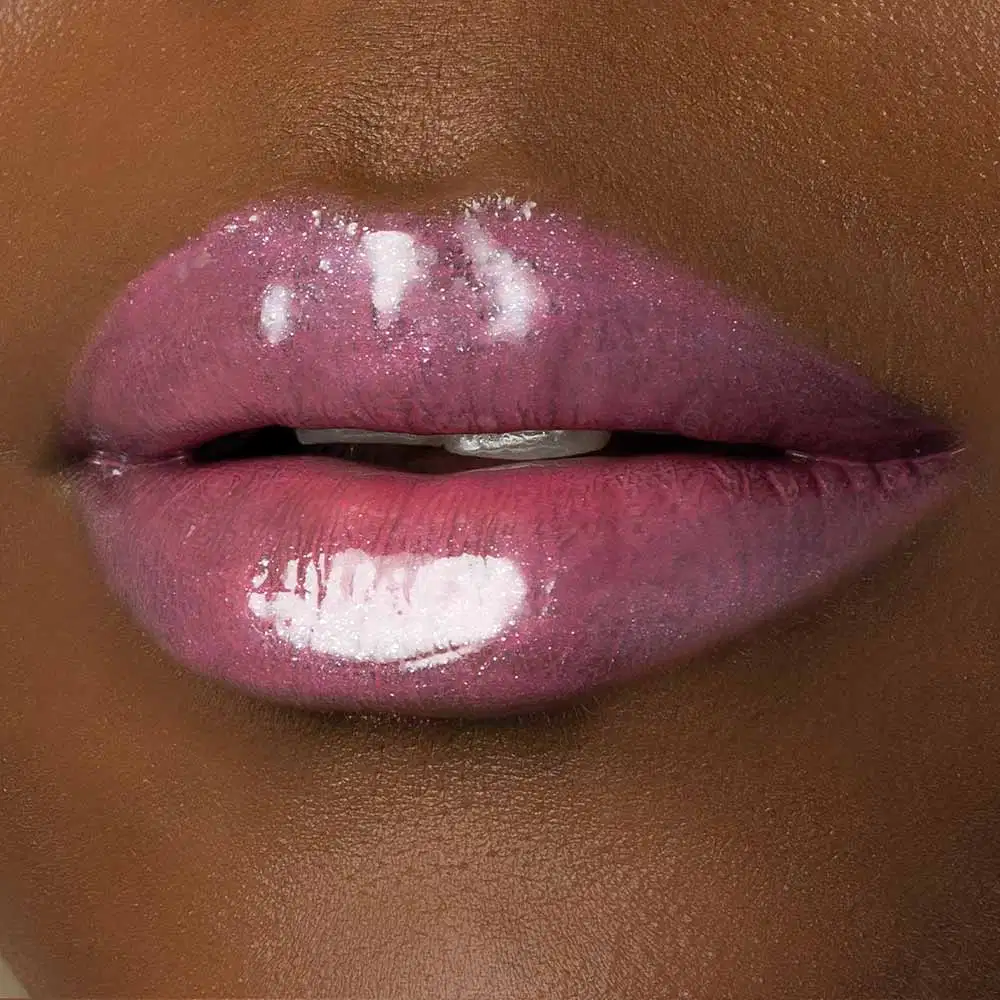 Close-up de um rosto feminino de pele negra evidenciando os lábios brilhantes e rosados que usam o gloss labial Rose Lover da marca Make B. 