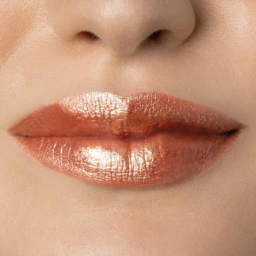 Close-up de um rosto feminino de pele negra evidenciando os lábios dourados e brilhantes, indicando o uso do batom líquido Diamond Dourado Luxury da marca Make B.