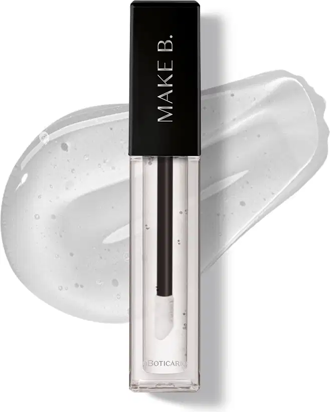 Gloss labial Incolor Crystal Icon da marca Make B. em frasco retangular transparente com líquido brilhante e sem cor e tampa preta com logo da marca, exibido sobre superfície branca com aplicação do produto ao fundo mostrando textura e acabamento.