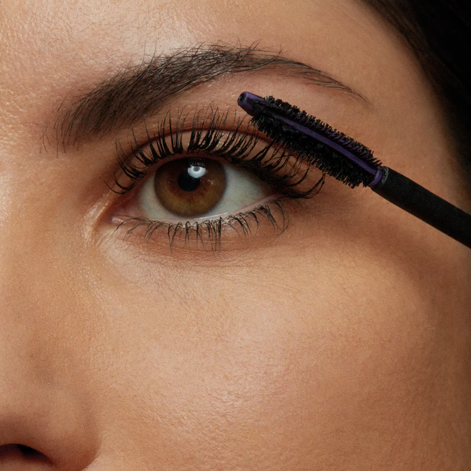 Close-up de um rosto feminino evidenciando os olhos, onde uma escova aplicadora aplica a máscara de cílios Make B. 4K Panoramic nos cílios, deixando os fios alongados e bem definidos.