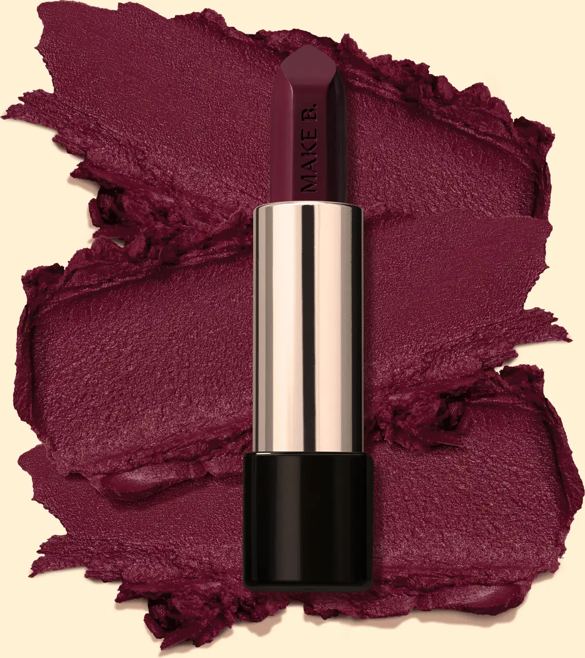 Batom cremoso na cor Vinho Fashion Berry da marga Make B., em tubo prateado com a parte inferior preta posicionado sobre amostra cremosa do produto na cor vinho intenso, sobre fundo bege claro.
