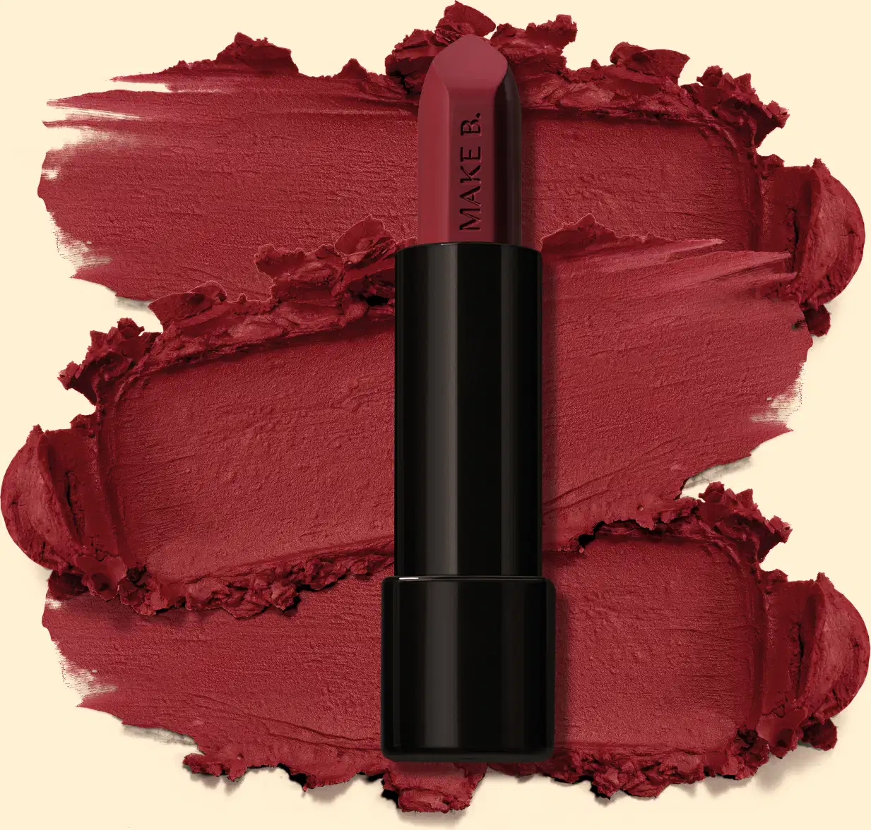 Batom mate na cor Vermelho Red Supreme da marga Make B., em tubo preto posicionado sobre uma amostra do produto na cor vermelho intenso, sobre fundo bege claro.