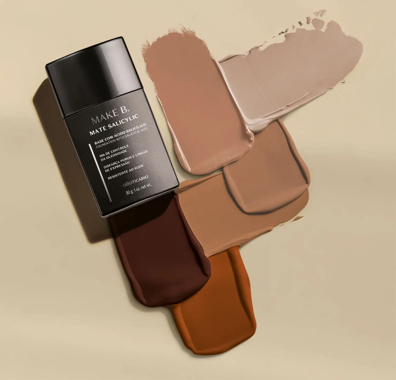 Frasco preto de base líquida Make B. Mate Salicylic ao lado de swatches de todos os tons do produto sobre superfície bege claro.