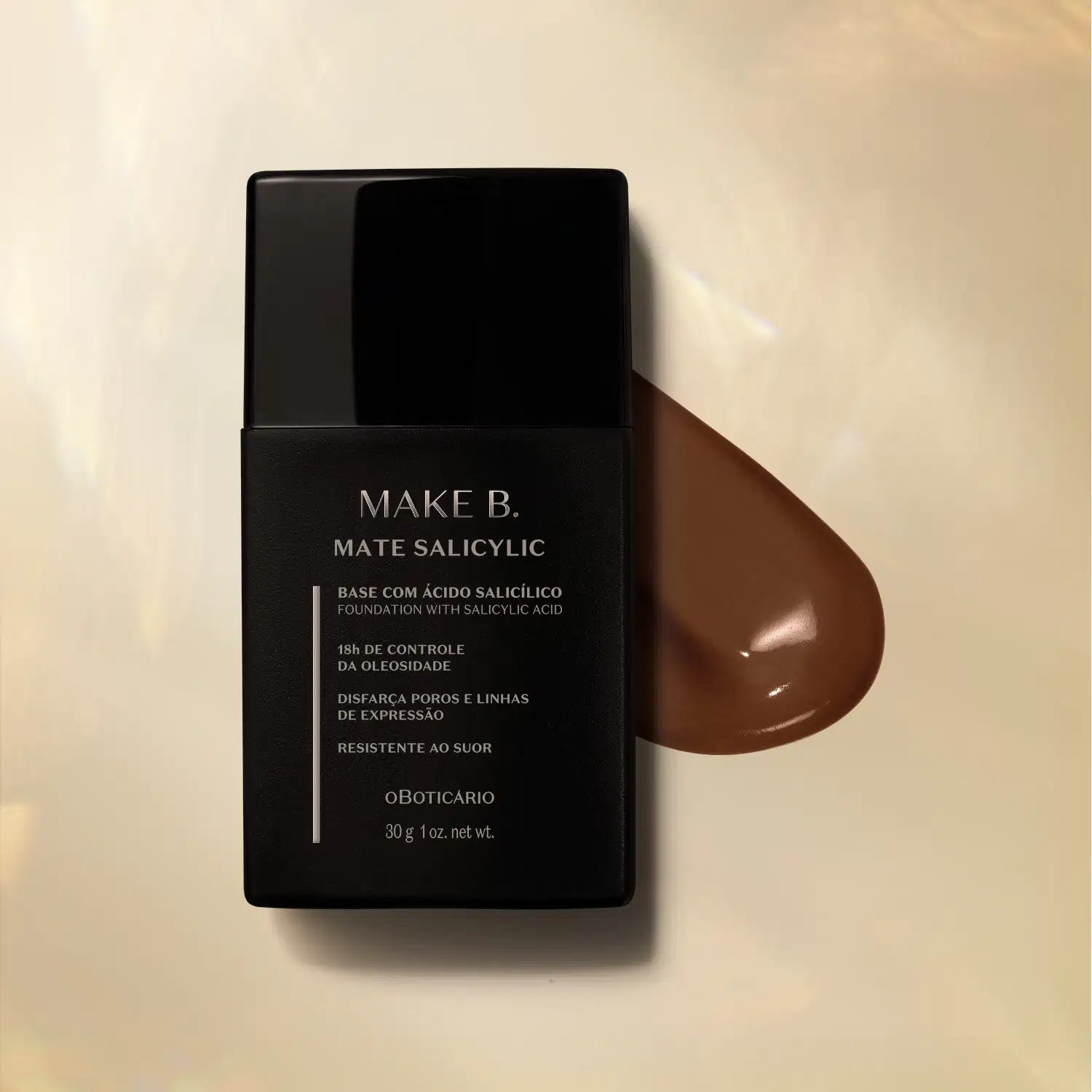 Frasco preto com letras cinzas de base líquida na cor 300 da marca Make B. Mate Salicylic sobre superfície bege com gota de produto marrom escuro ao lado, mostrando textura e tonalidade.