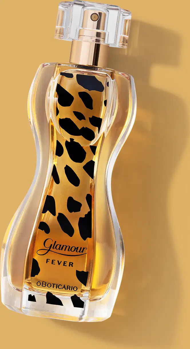 Vidro transparente com formato curvilíneo e líquido âmbar, borrifador dourado, tampa cristal e rótulo com estampa de animal print de desodorante colônia Glamour Fever sobre fundo bege com sombra, spray prateado no topo e líquido âmbar visível.
