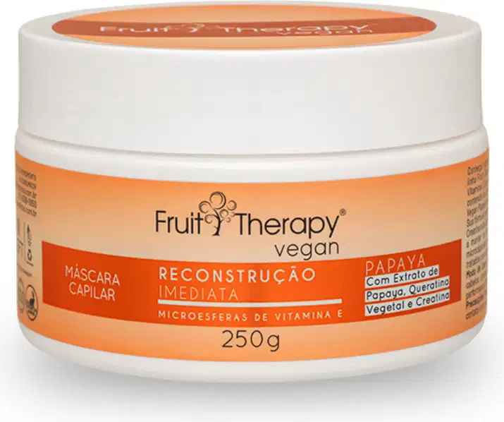 A imagem mostra a máscara de reconstrução da linha Fruit Therapy Vegan de Papaya. Ela é embalada em um pote plástico branco de 250g. O rótulo tem um fundo laranja e destaca os benefícios do produto.