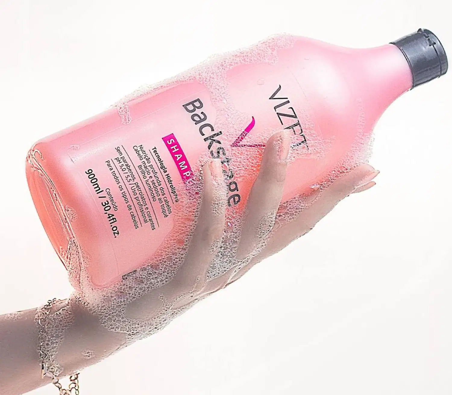 A imagem mostra uma mão ensaboada segurando o frasco com o shampoo.