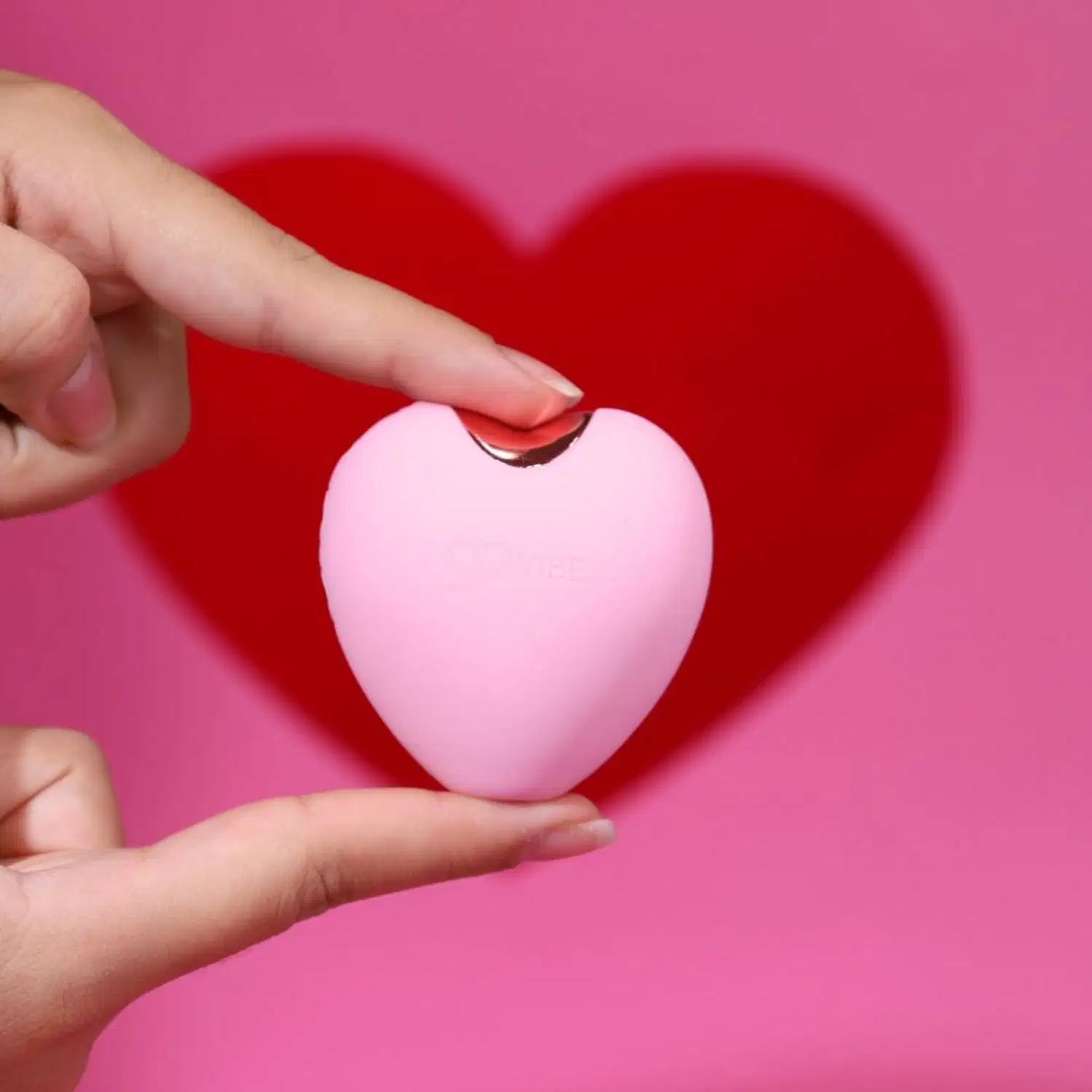 Mão segurando o Estimulador de Clitóris Recarregável Go Vibe Love sobre fundo rosa com coração vermelho