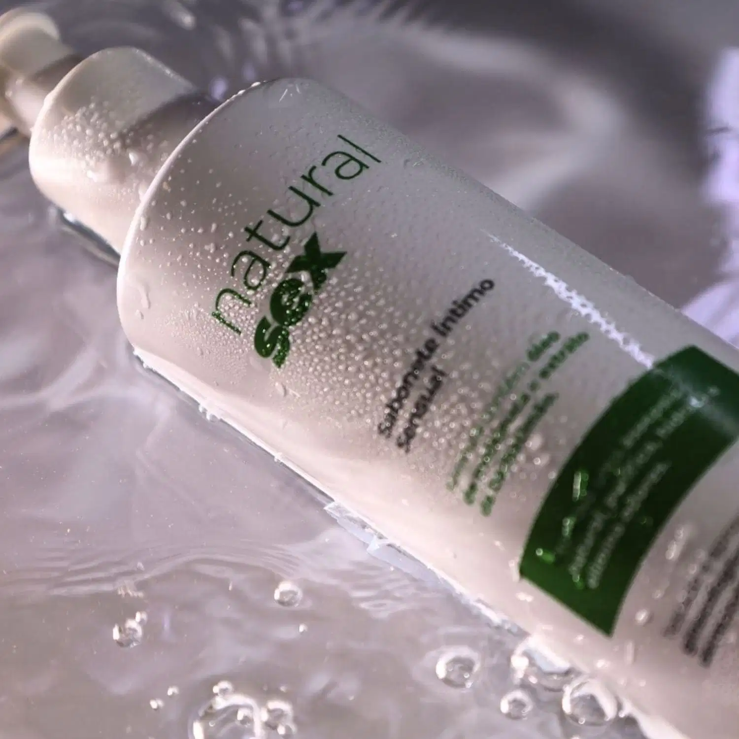Sabonete Íntimo Líquido Natural Sex, com fundo repleto de gotas de água visíveis na superfície