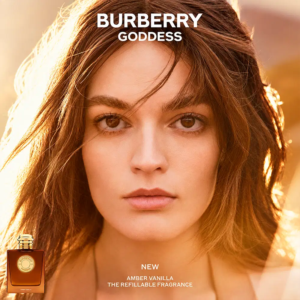 Ambiente aquecido com tons âmbar e dourados, iluminação natural suave que destaca a elegância do frasco. Cenário sofisticado apropriado para uso diário refinado, refletindo a essência luxuosa da marca Burberry.