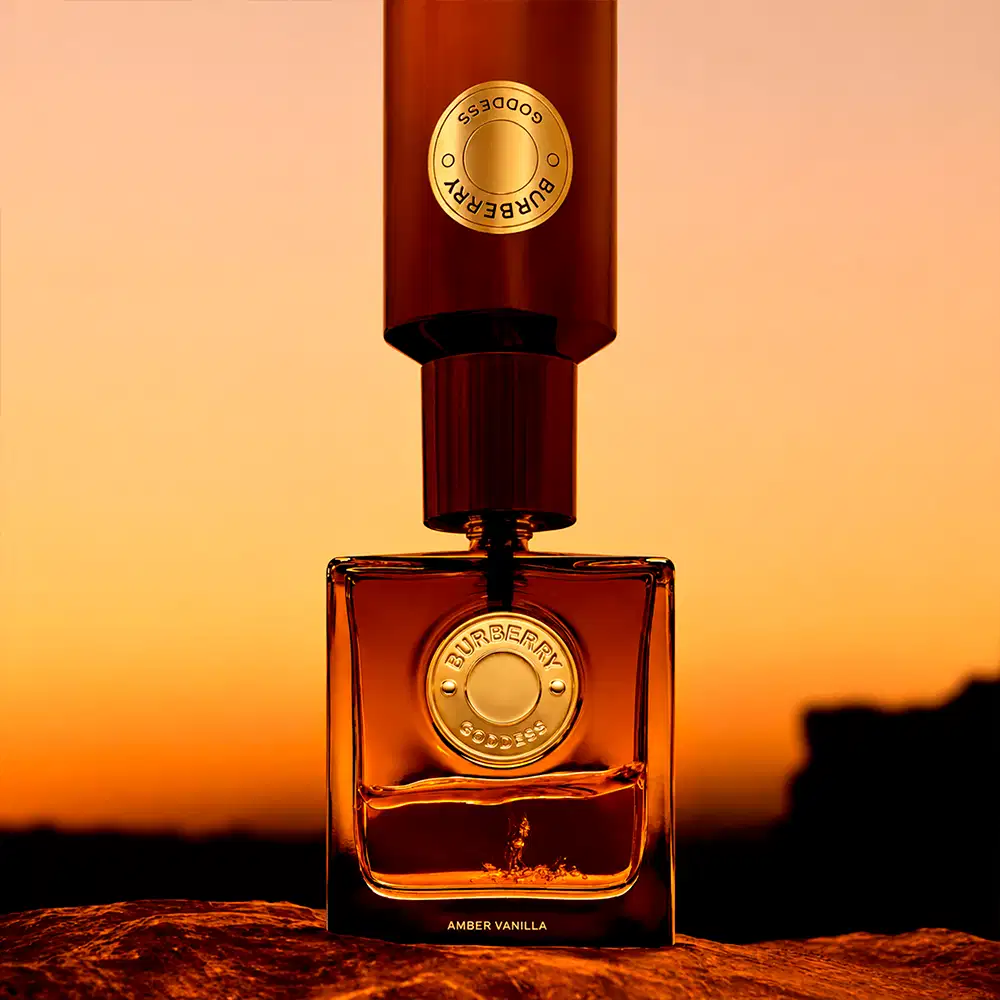 Perfume Burberry Amber Vanilla em frasco quadrado de vidro âmbar com tampa cilíndrica marrom e aplicador. Rótulo dourado com brasão Burberry. Embalagem elegante e sofisticada com acabamento premium.