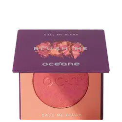 A imagem mostra o produto Blush Me da marca Océane. É uma embalagem quadrada de cor roxa que está semiaberta mostrando a cor do blush em um tom laranja com leve brilho perolado. A parte interna da embalagem é de cor pêssego claro,