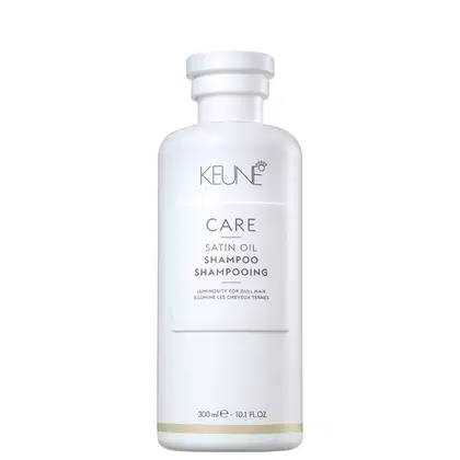 Frasco branco de shampoo da marca Keune Care, com rótulo em letras pretas indicando "Satin Oil Shampoo". O produto é apresentado em embalagem cilíndrica com tampa branca.