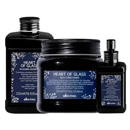 Conjunto de produtos Davines Heart of Glass, incluindo shampoo, condicionador e spray brilhante, em embalagens pretas com detalhes florais azuis, apresentando informações sobre os benefícios para cabelos loiros.