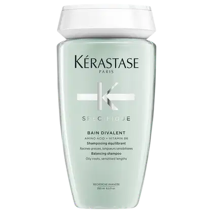 Frasco de plástico com tampa branca. Rótulo verde claro com texto "KÉRASTASE PARIS" e "SPECIFIQUE BAIN DIVALENT" em preto. Produto de cuidados capilares para equilibrar raízes oleosas e pontas sensibilizadas.