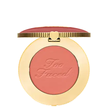 Blush compacto de maquiagem com embalagem redonda dourada. A tampa superior é rosa com a inscrição "Too Faced" em letras cursivas. Um pequeno coração dourado adorna o centro da tampa.