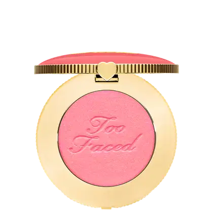 Blush compacto de maquiagem com embalagem redonda dourada. A tampa superior é rosa com a inscrição "Too Faced" em letras cursivas. Um pequeno coração dourado adorna o centro da tampa.
