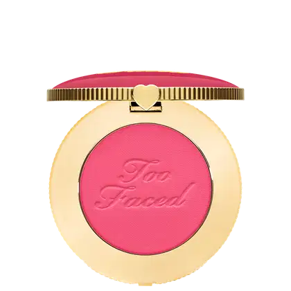 Blush compacto de maquiagem com embalagem redonda dourada. A tampa superior é rosa com a inscrição "Too Faced" em letras cursivas. Um pequeno coração dourado adorna o centro da tampa.