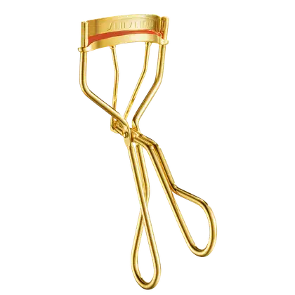 Produto de maquiagem da marca Shiseido. Objeto dourado em forma de curvador de cílios. Possui uma faixa vermelha com o nome "Shiseido" gravado em letras maiúsculas.
