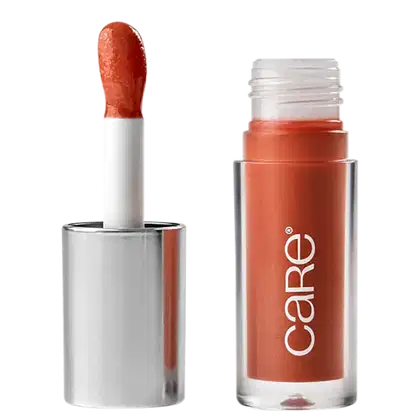 A imagem mostra o Lip Oil de Care Natural Beauty. Possui uma embalagem transparente de plástico, semelhante a um batom líquido. Possui cor pêssego e a embalagem apresenta o logotipo "Care" em letras brancas. A tampa prata com aplicador.