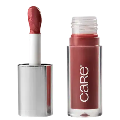 A imagem mostra o Lip Oil de Care Natural Beauty. Possui uma embalagem transparente de plástico, semelhante a um batom líquido. Possui cor marrom e a embalagem apresenta o logotipo "Care" em letras brancas. A tampa prata com aplicador.