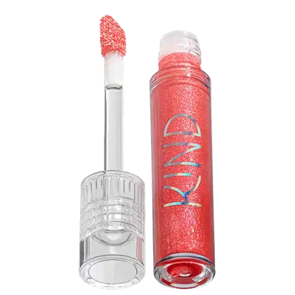 A imagem mostra a tampa da embalagem do gloss, com o aplicador virado pra cima, semelhante a uma tampa de batom, transparente e cilíndrica. Ao lado, o frasco do gloss, com o produto de cor coral e com a palavra KIND escrito na embalagem.