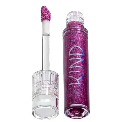A imagem mostra a tampa da embalagem do gloss, com o aplicador virado pra cima, semelhante a uma tampa de batom, transparente e cilíndrica. Ao lado, o frasco do gloss, com o produto de cor roxa e com a palavra KIND escrito na embalagem.