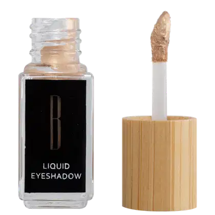 A imagem mostra um frasco aberto, retangular, transparente ao lado do aplicador de rosquear e com a ponta com a cor da sombra líquida, bege claro. O rótulo do frasco é preto com logo da marca em dourado e "Liquid Eyeshadow" em branco no rodapé.