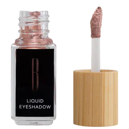 A imagem mostra um frasco aberto, retangular, transparente ao lado do aplicador de rosquear e com a ponta com a cor da sombra líquida, rosa. O rótulo do frasco é preto com logo da marca em dourado e "Liquid Eyeshadow" em branco no rodapé.