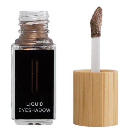 A imagem mostra um frasco aberto, retangular, transparente ao lado do aplicador de rosquear e com a ponta com a cor da sombra líquida, bronze. O rótulo do frasco é preto com logo da marca em dourado e "Liquid Eyeshadow" em branco no rodapé.