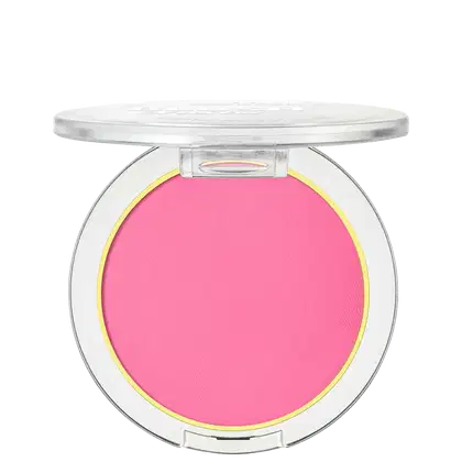A imagem mostra um blush compacto de cor rosa pink em uma embalagem plástica transparente. O blush tem um acabamento fosco e está disposto em um estojo redondo. Em volta do pó compacto rosa, há um aro amarelo que realça a cor do produto.