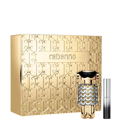 Conjunto de produtos Rabanne. Caixa dourada decorada com padrão geométrico vazado e nome "Rabanne" gravado. Frasco de perfume dourado com detalhes prateados e pretos, formato de robô estilizado. Máscara de cílios em embalagem prata com degradê preto.