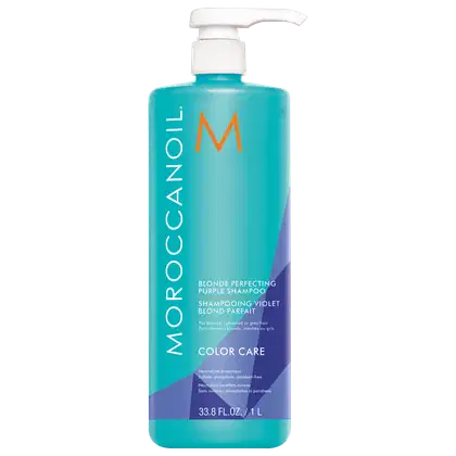 A imagem mostra o Shampoo Moroccanoil Color Care Blonde Perfecting 1L, um frasco cilíndrico azul claro com detalhes em roxo e laranja e aplicador pump branco. De acordo com as informações na embalagem, tem a função de neutralizar os tons amarelados.
