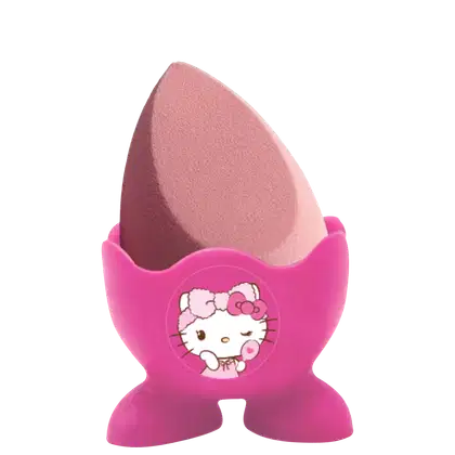 Esponja de maquiagem em formato de gota com uma base plástica rígida rosa escuro que lembra uma casca de ovo pela metade. Na frente, temos uma ilustração da Hello Kitty em branco com detalhes rosa.